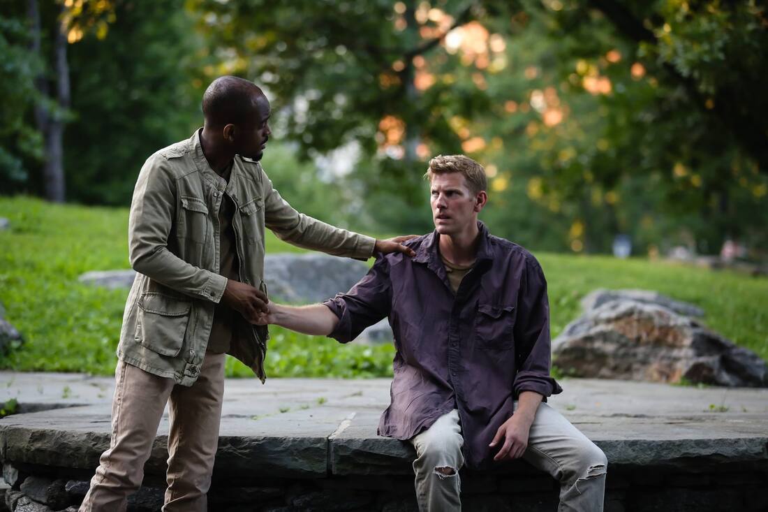 Production photo from Bethel Park Falls of a standing man shaking hands with a seated man outside in a park.