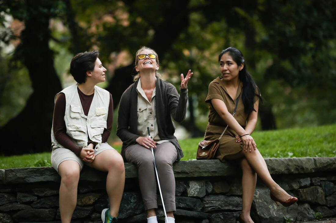 Production photo from Bethel Park Falls of three cast members seated on a low stone wall outside, as the middle woman turns her face to the sky.