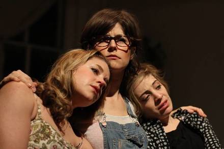 Production photo of two women leaning on the shoulders of a woman in the middle, in When I Had Three Sisters by Jason Pizzarello